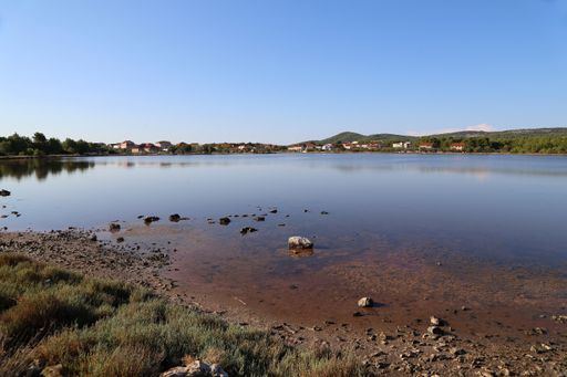 A landscape of a salty lake surrounded by greenery and buildings under a blue sky in Croatia