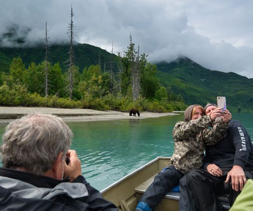A group of people on a boat taking a selfie with a bare on the background in green mountains