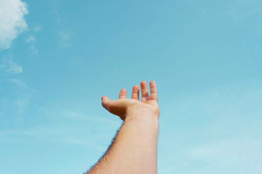 A side profile of a human hand stretching up towards the sky on a bright and sunny day