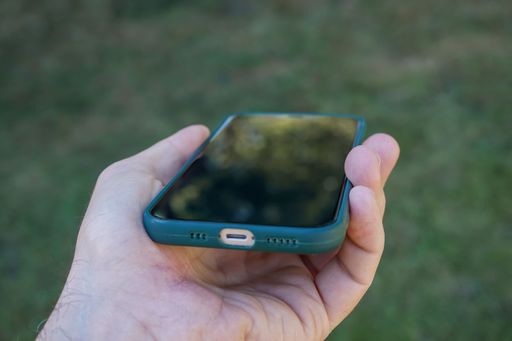 An adult person holds an open green smartphone device in their right hand, looking towards the camera