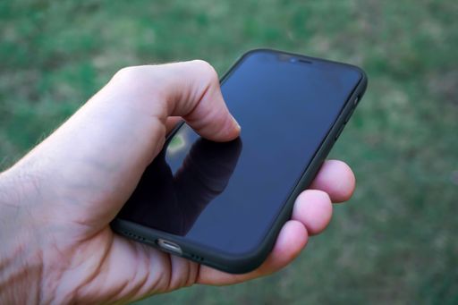 A young adult stands outdoors in the sunlight, holding an iPhone in their hand