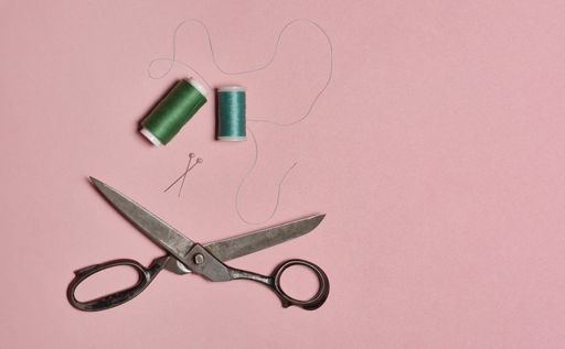 A high angle shot of sewing threads, pins and scissors on a pink background