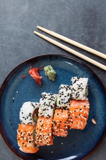A vertical top view of a pair of chopsticks over a plate of gourmet sushi rolls