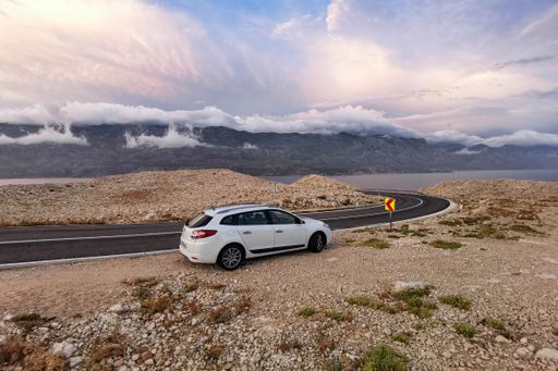 A closeup view of the car parked next to the empty highway surrounded by hills on a sunny summer day