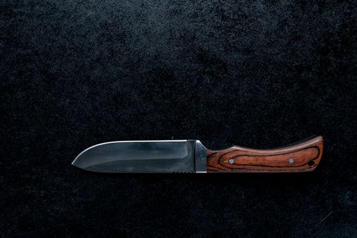A closeup shot of a small sharp knife with a brown handle  on a black background