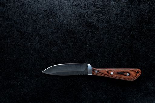 A closeup shot of a small sharp knife with a brown handle  on a black background