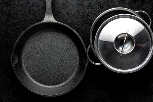 A black metal frying pan and a pot with a glass lid on a black background