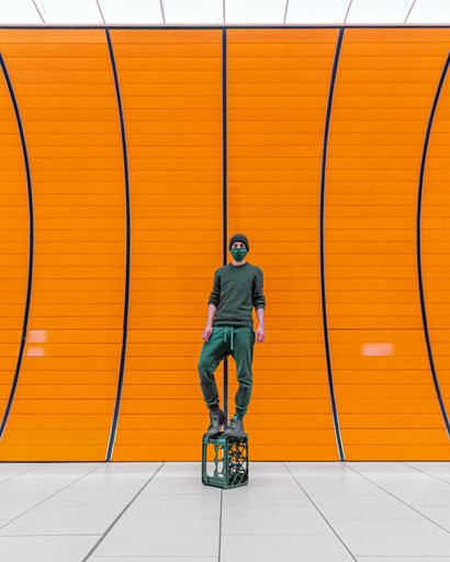 A Caucasian male wearing safety goggles stands in front of an orange wall in a brightly lit room