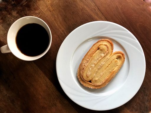 A top view of a biscu with powdered sugar and black coffee in a mug on the wooden table