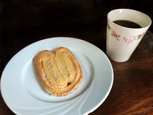 A top view of a biscuit with powdered sugar and black coffee in a mug on the wooden table