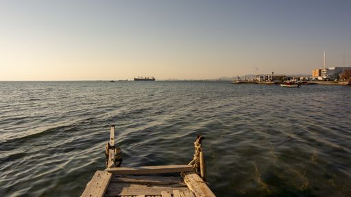 A closeup shot of a deck leading to the sea with a harbor in the background