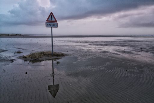 A sign on a metal pole put on the beach under a cloudy sky