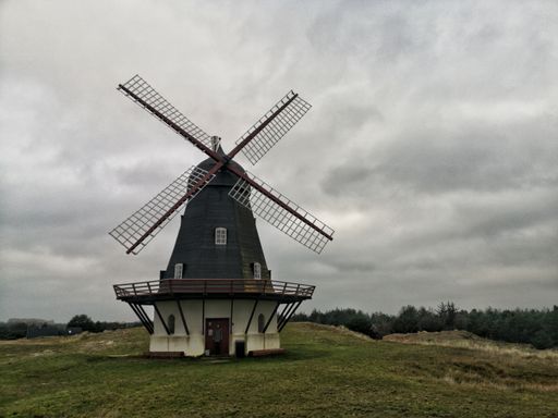 A wide angle shot of a windmill under a sky full of clouds