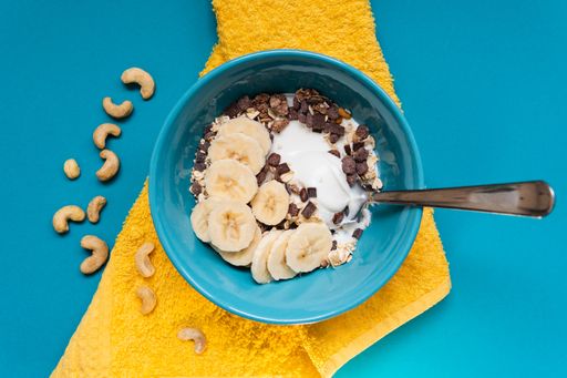 A bowl of healthy cereal with yogurt and bananas on a blue table