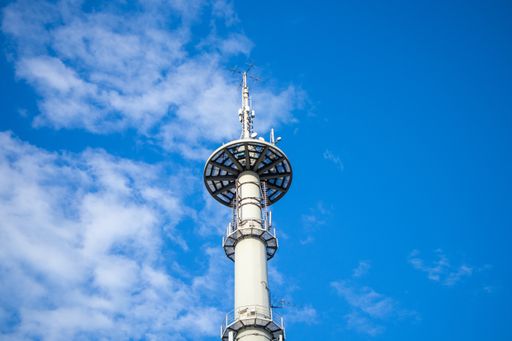 A communication tower in the middle of the picture with a partly cloudy sky.