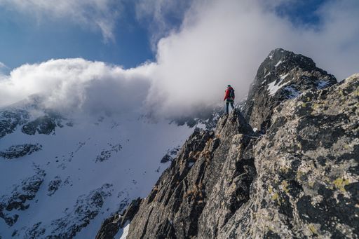 An alpinist standing on top of a high rock and watching winter mountain alpine landscape. Hiker or climber on an adventure ascent to the summit.
