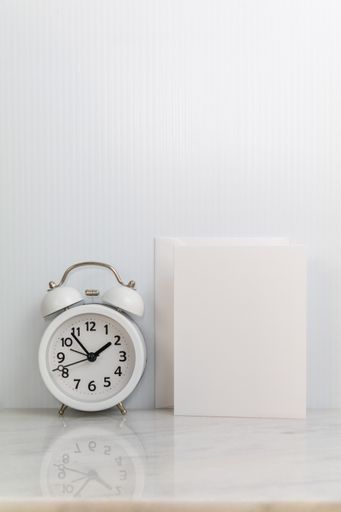 A vertical shot of a classically designed alarm clock beside a box lamp on white background