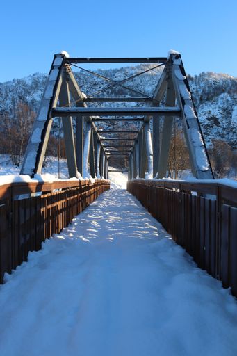 A vertical shot of a bridge covered in snow under a clear blue sky