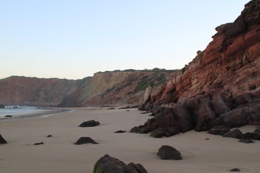A stunning beach with a rocky coastline, situated near a cliff face, with the tranquil ocean waters in the background