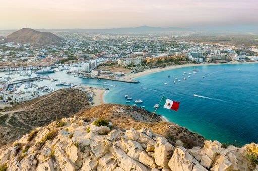 A vibrant flag waving in the foreground of a picturesque cityscape. Cabo San Lucas, Mexico.