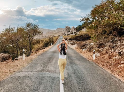 A brunette adult woman walking through a highway in the countryside under a cloudy sky
