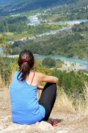A young female sitting atop a large rock, enjoying the breathtaking scenery
