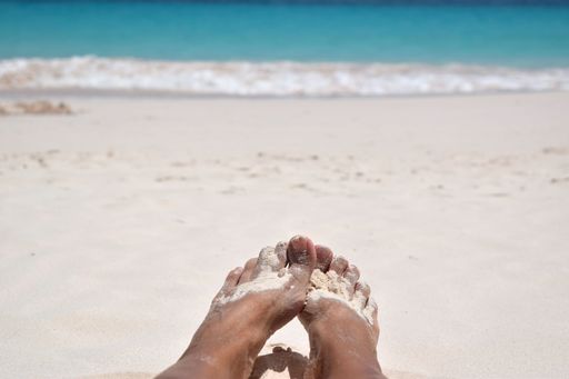 A closeup view of person's feet covered in sand on the beach in sunny weather