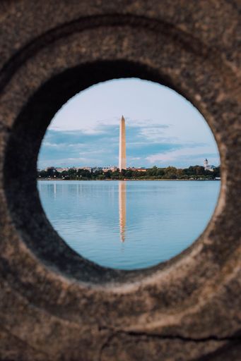 A vertical shot of the Washington Monument reflected in the waters of a lake against the blue sky
