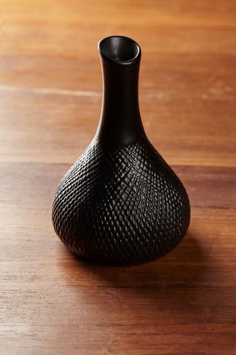 A  vertical shot of a unique black bottle on a wooden table