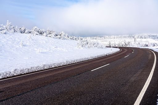 A scenic winter scene featuring a winding road located at the bottom of a hill