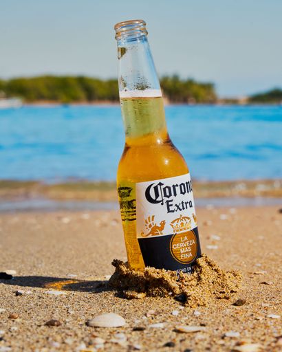 A  vertical shot of a bottle of Corona Extra beer   in a sandy beach