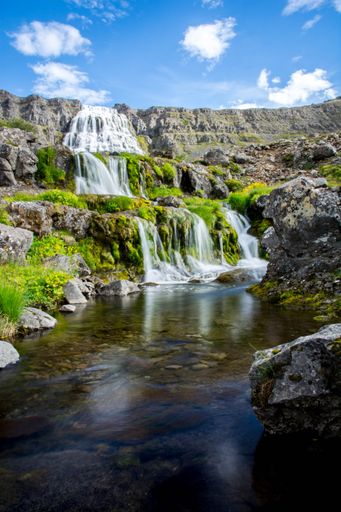 The waterfall flowing over the large rocks with grass nearby