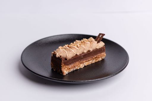 A black ceramic plate with a rich, chocolate cake topped with a layer of creamy, white frosting