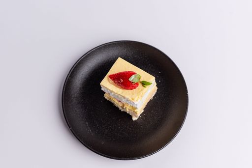 A delicious piece of white Shortcake on a black plate, decorated with fresh red strawberries on a white background
