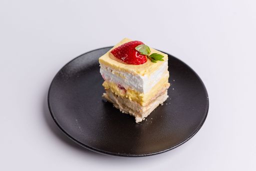A delicious piece of white Shortcake on a black plate, decorated with fresh red strawberries on a white background