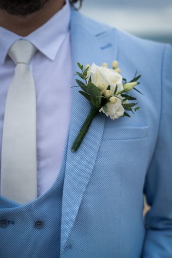 A closeup shot of grooms light blue suit and a small white flower on it
