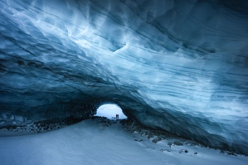 Silhouettes of a couple of hikers at the entrance of an ice cave with shades of blue and textures in Zermatt