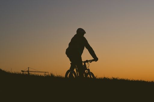 The silhouette of a person riding a bicycle on a field during a sunset