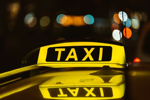 A black and yellow sign of Taxi at night placed on top of a car