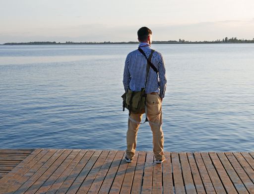 A vertical shot of a man standing on a wooden border and admiring the sea view