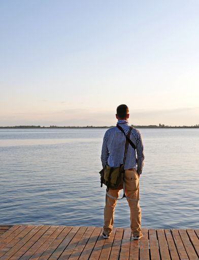 A vertical shot of a man standing on a wooden border and admiring the sea view