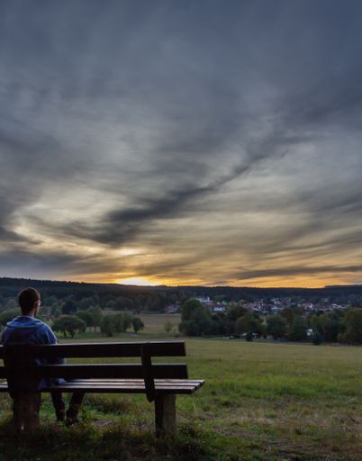 A vertical shot of a person sitting on a bench under a sky full of clouds