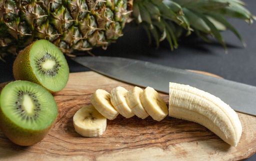 Kiwis, banana and a pineapple put on a cutting board next to each other