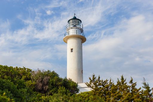 A low angle shot of a lighthouse on background of the cloudy blue sky seen through trees