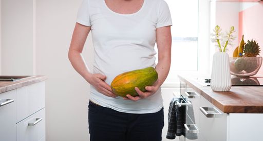 A pregnant woman in a white shirt holding papaya in her hand