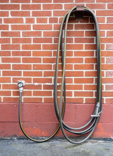 A vertical shot of a garden hose hanging from a brick wall