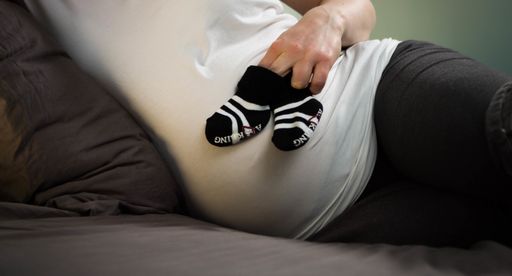 A beautiful shot of a pregnant woman in bed holding baby shoes in front of her belly