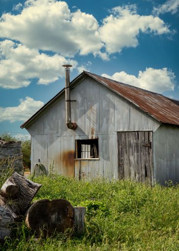 A vertical shot of an old barn in a field with a weathered roof under a cloudy sky