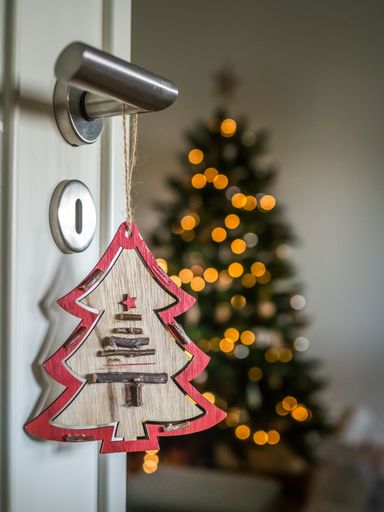 A tree ornament hanging from the knob of the door with a Christmas tree on the blurry background