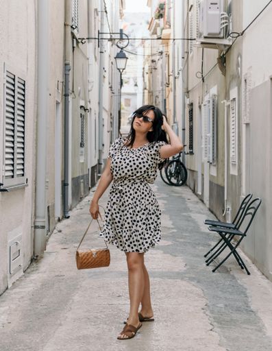 A shallow focus of an adult woman wearing a dress with polka dots and posing on an alley